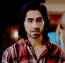 a man with long hair and a beard wearing a plaid shirt looks at the camera