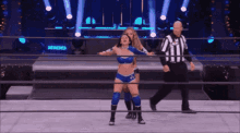a woman is standing in a wrestling ring with a referee behind her