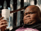 a fat man is holding a styrofoam cup in his hand and making a funny face .