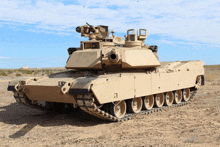 a military tank is parked in a dirt field with a blue sky behind it
