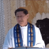 a man in a white robe with a blue and orange scarf around his neck is reading a book