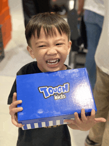 a young boy is holding a blue tough kids shoe box