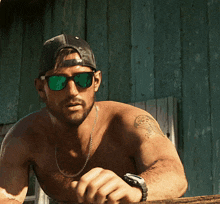 a shirtless man wearing sunglasses and a hat has a tattoo on his arm