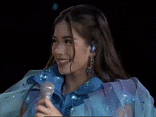 a woman in a blue dress is holding a microphone and smiling on a stage .