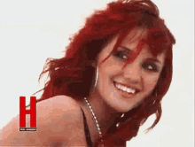 a woman with red hair is smiling with the letter h in the background