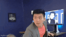 a man in a suit and tie is standing in front of a computer screen .