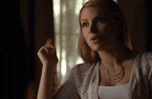 a woman wearing a white sweater and a gold necklace is sitting in front of a window