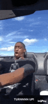 a man is sitting in the driver 's seat of a car with the words turnnn up on the bottom