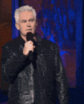 a man in a leather jacket stands in front of a microphone with the words get a dictionary above him