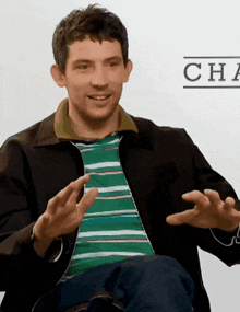 a man wearing a green and white striped shirt and a black jacket has his hands out