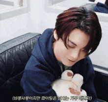 a man in a blue hoodie is holding a stuffed animal in his lap