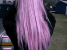 a woman with long pink hair is standing next to a car in a parking lot .
