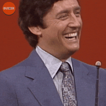 a man in a suit and tie is laughing in front of a microphone with the buzzr logo in the corner