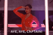 a woman in a red jumpsuit is standing in front of a screen and says aye aye captain .