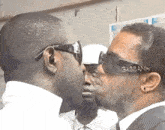 a man wearing gabbana sunglasses kisses another man on the cheek .