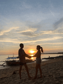 two people holding hands on a beach at sunset with boats in the background