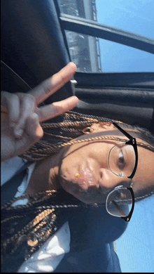 a girl wearing glasses and braids giving a peace sign