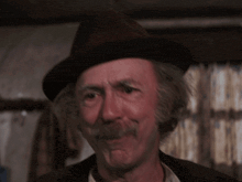 a man wearing a hat and a mustache says but it can be done