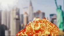 a statue of liberty is in the background of a blurry picture of a city with a fireball in the foreground .