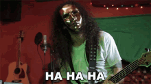 a man with a mask on his face is playing a bass guitar with the words ha ha ha written below him