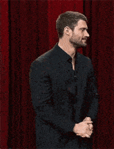 a man in a suit and tie is standing on a stage in front of a red curtain .