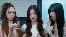 three girls are standing next to each other and one of them is holding a piece of cake