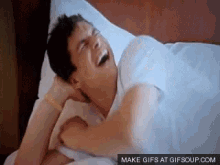 a man is laughing while laying in bed with a pillow .