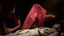 a man in a suit is laying on a bed while a woman in a red veil stands behind him