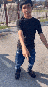 a young man in a black shirt and jeans is standing on a sidewalk pointing at something .