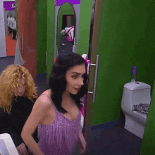 a woman in a purple dress stands in front of a toilet in a bathroom