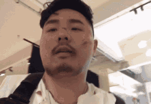 a man with a beard is wearing a white shirt and a black necklace