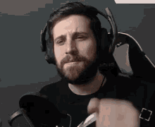 a man with a beard is wearing headphones and a microphone while sitting in a chair .