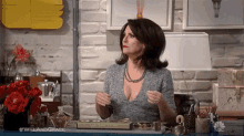 a woman is sitting at a desk in front of a brick wall holding her breasts .