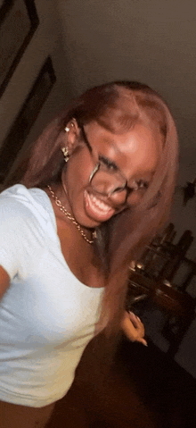 a woman wearing glasses and a white shirt is taking a selfie in a room .