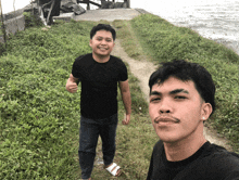 two men standing next to each other with one giving a thumbs up sign