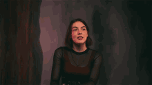 a woman in a black top stands in front of a purple background