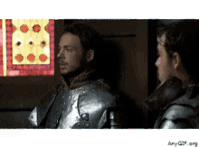 a man in armor stands next to another man in a black jacket