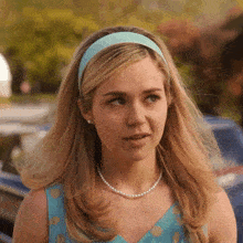 a woman wearing a blue headband and pearls looks to the side