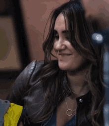 a woman wearing a leather jacket and a necklace smiles for the camera