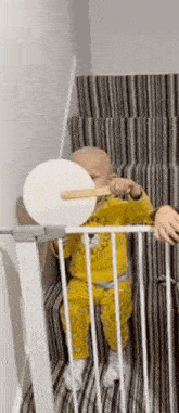 a baby is sitting on a set of stairs behind a fence holding a toy .