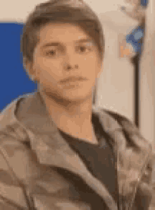 a young man in a camo jacket is looking at the camera .