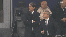 a group of men sitting in a stadium watching a soccer game sponsored by sky sport
