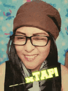 a woman wearing glasses and a beanie is smiling and making a funny face .