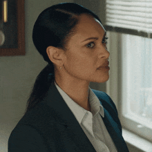 a woman in a suit and white shirt looks out of a window
