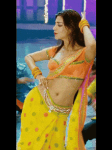 a woman in a yellow and orange polka dot saree is dancing