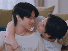 a man wearing a white shirt with the word floral on it is being hugged by another man