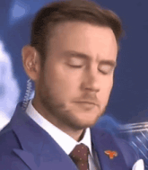 a man wearing a blue suit and tie with his eyes closed and ear plugs