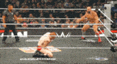 a wrestler is kneeling down in a wrestling ring while another wrestler stands behind him