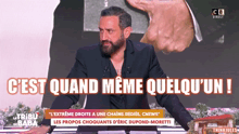 a man with a beard is standing in front of a sign that says c'est quand meme quelqu ' un