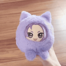 a person is holding a purple stuffed animal with a cat head